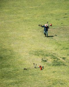 High Angle Shot of a Man Walking on a Grass Field with a Grass Trimmer